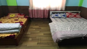 A room with two beds, one with a floral bedspread and the other with a checkered bedspread. There is a window with sheer curtains, and the room has a wooden floor. - MeroStay 010 Miracle Hotel Lodge and Restaurant (Kathmandu)
