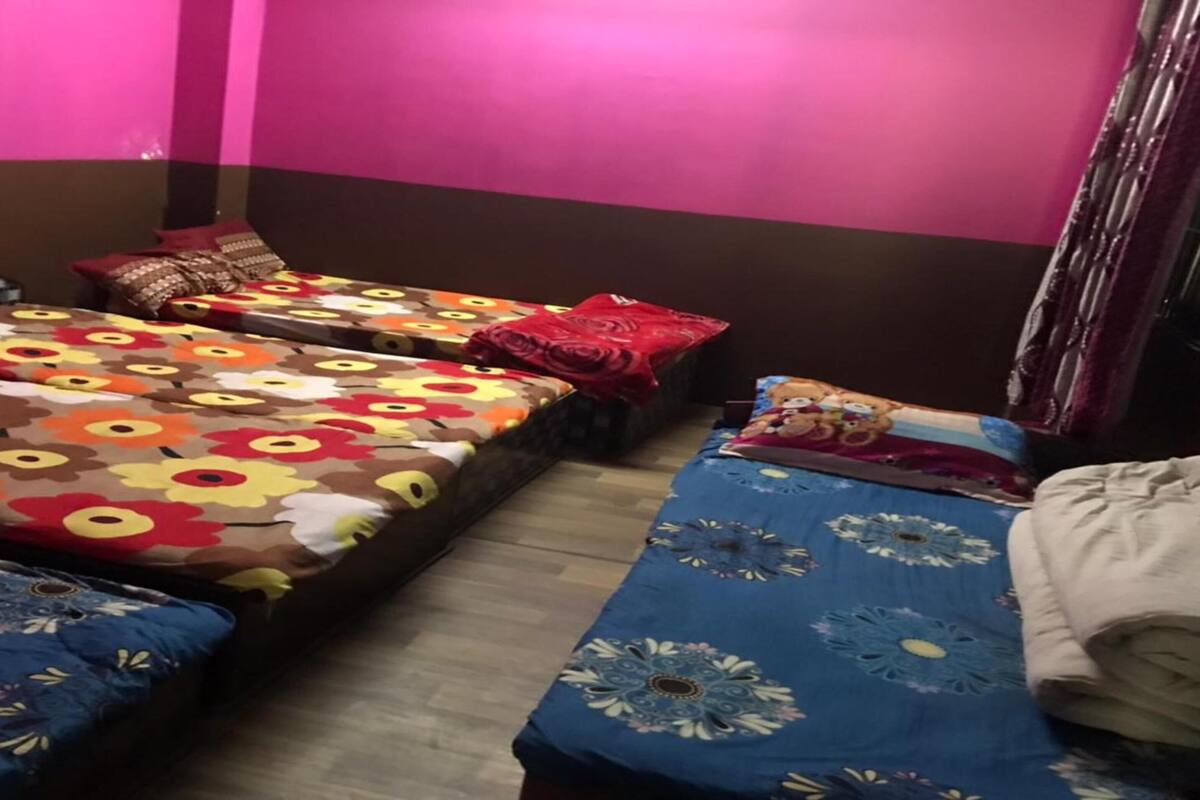 Ein Zimmer mit zwei Betten, jeweils mit einem blumigen Überwurf, einem Sessel und einem Vorhang.