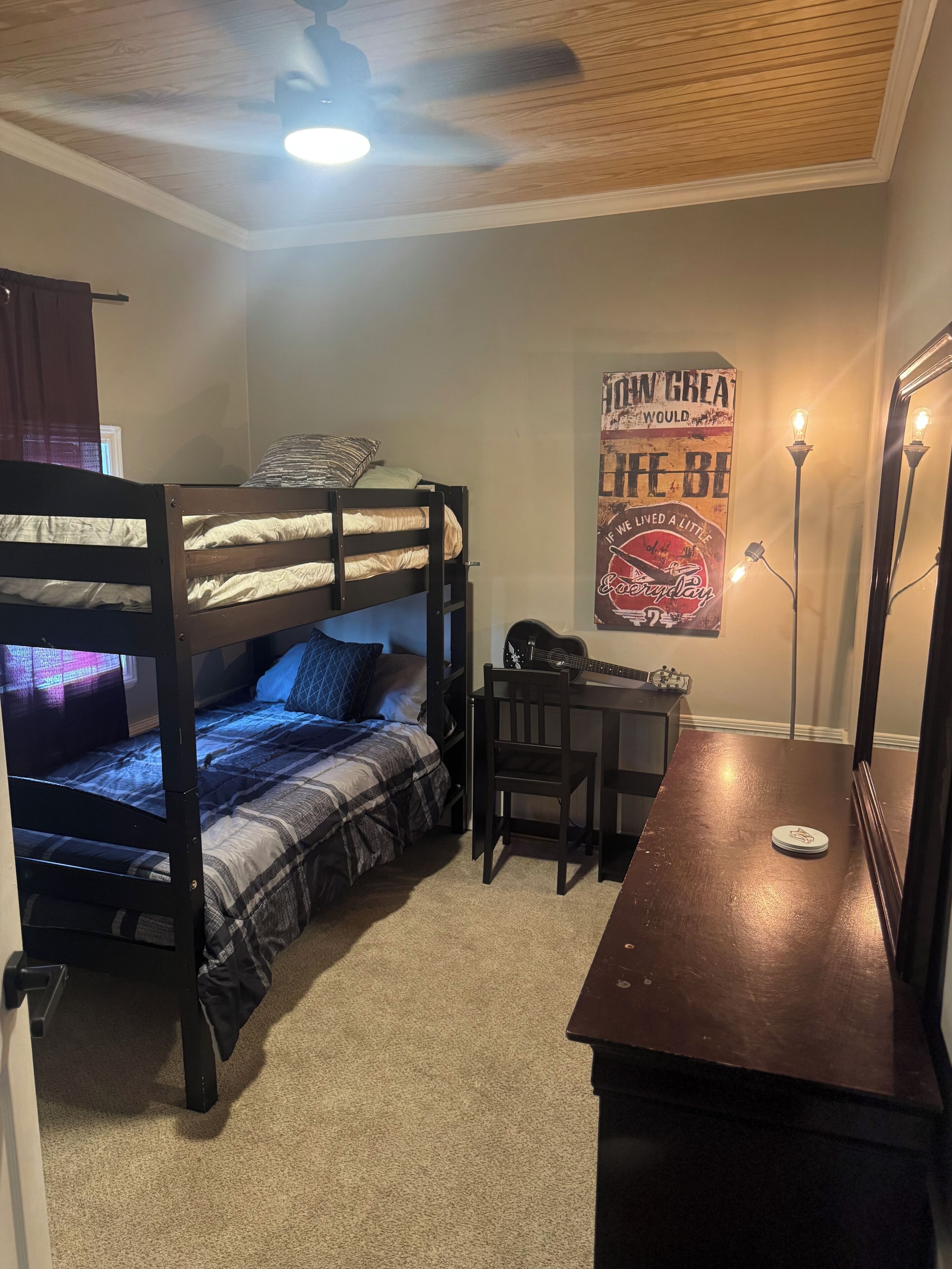 Habitación con literas, un escritorio, una silla, ventilador de techo y un póster en la pared.
