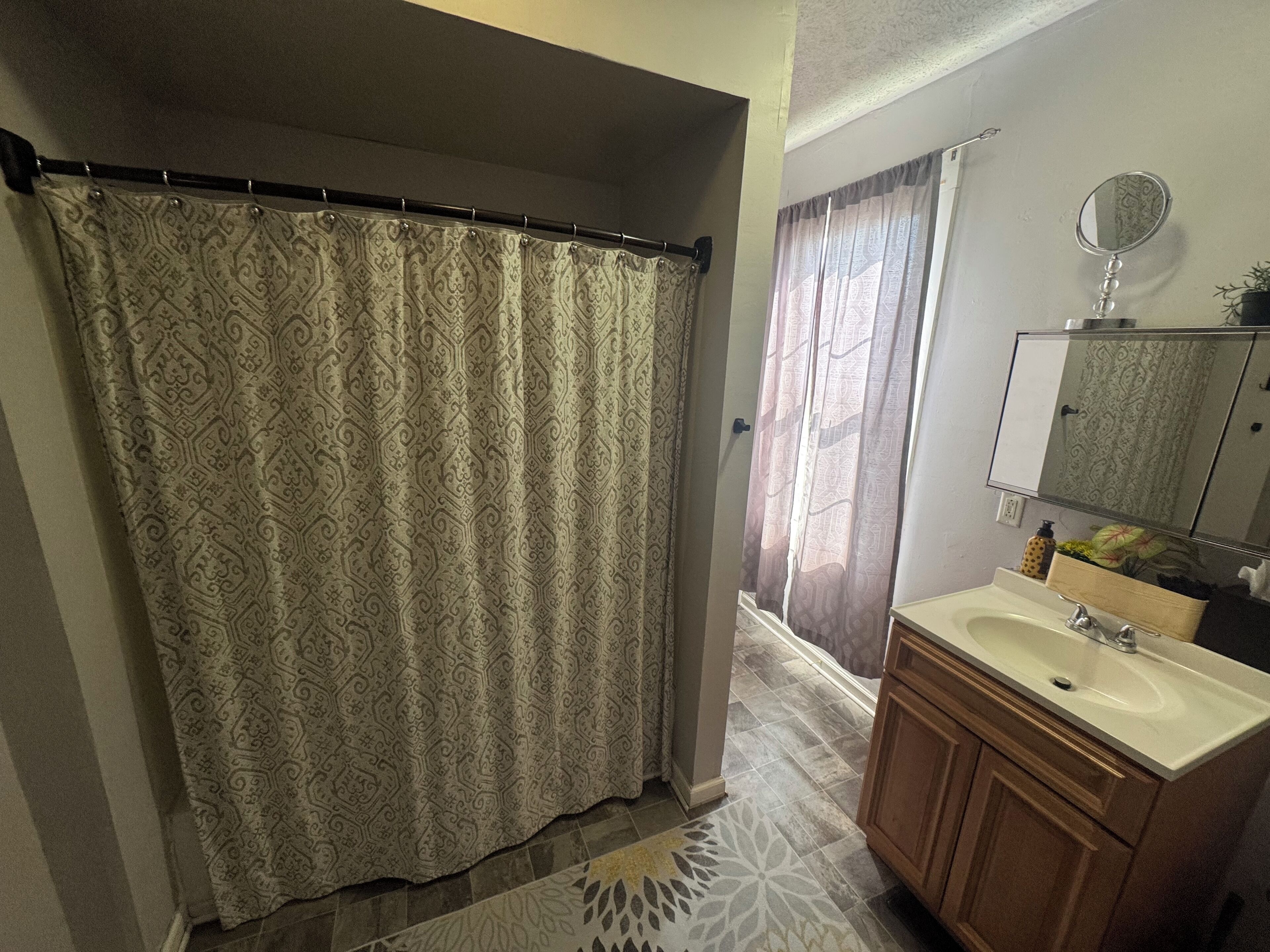 A bathroom with a patterned shower curtain, a sink with a mirror above it, and a patterned floor.
