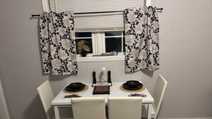 A dining area with a white table set for four, two chairs, and a window with curtains. - Rose Music House- 8 min from Broadway (Nashville)