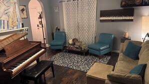 A living room with a grand piano, a blue armchair, a beige sofa, and a patterned rug. - Rose Music House- 8 min from Broadway (Nashville)
