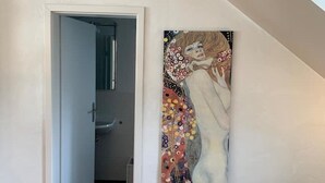 Una habitación con piso de madera, una puerta blanca que da a un baño y un cuadro grande en la pared.