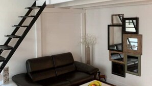 Una sala de estar moderna con un sofá de cuero negro, una mesa de centro blanca con fruta, una escalera y una zona superior tipo loft.