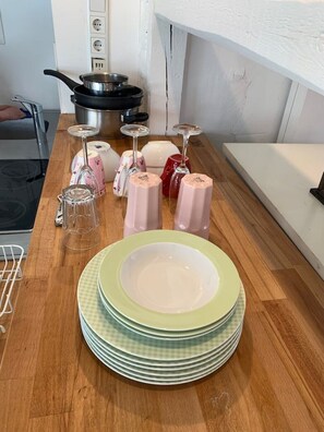 A kitchen counter with stacked plates, a frying pan, a kettle, and a few wine glasses.