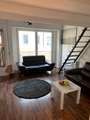 A living room with a black leather sofa, a white coffee table with fruit, a black rug, and a staircase.
