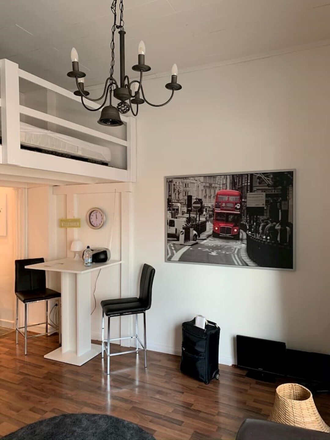 A modern living room with a loft bed, a dining area, a black chair, a black bag, and a black TV stand.
