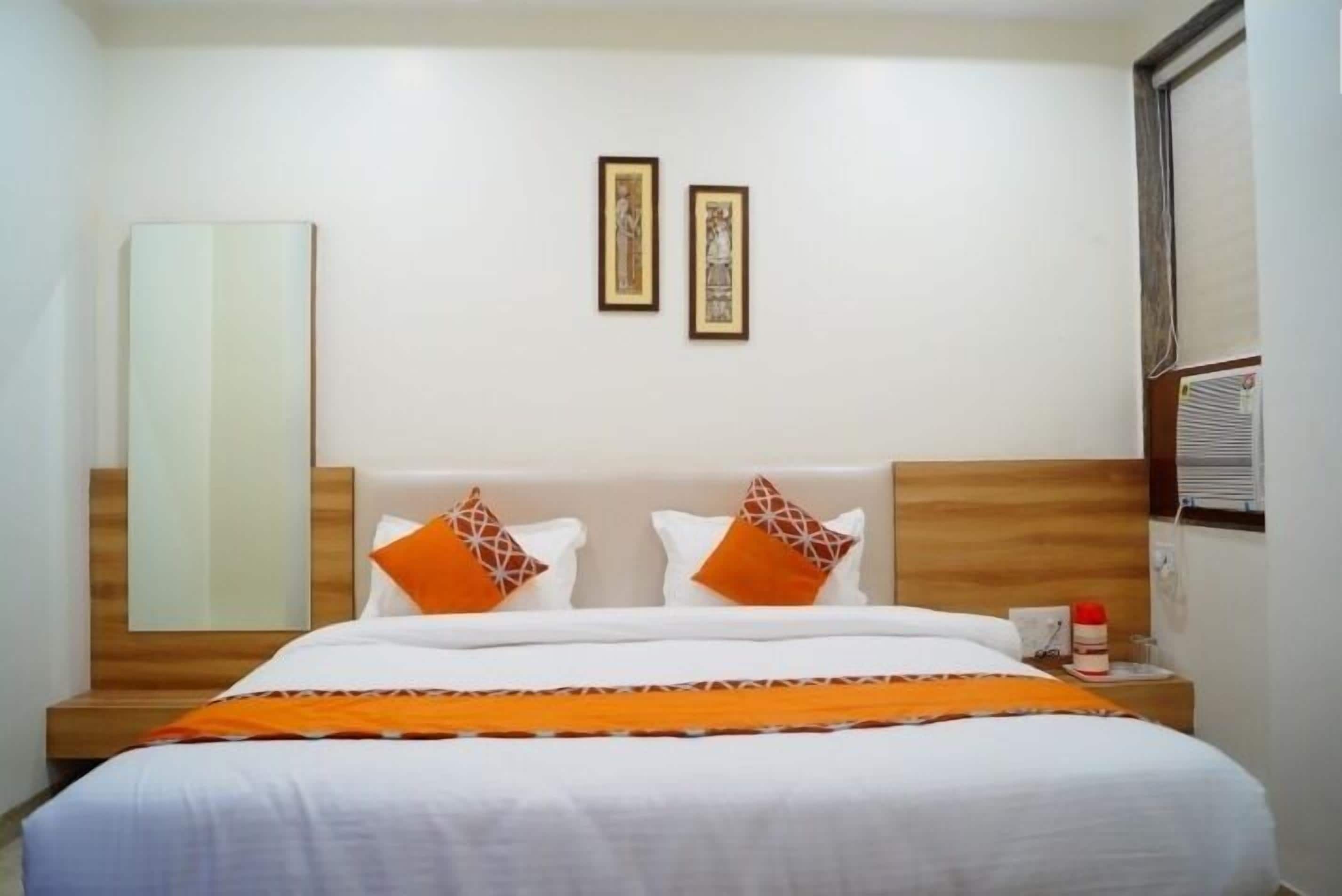 A neatly made bed with white and orange bedding, a wooden headboard, and two framed pictures on the wall.