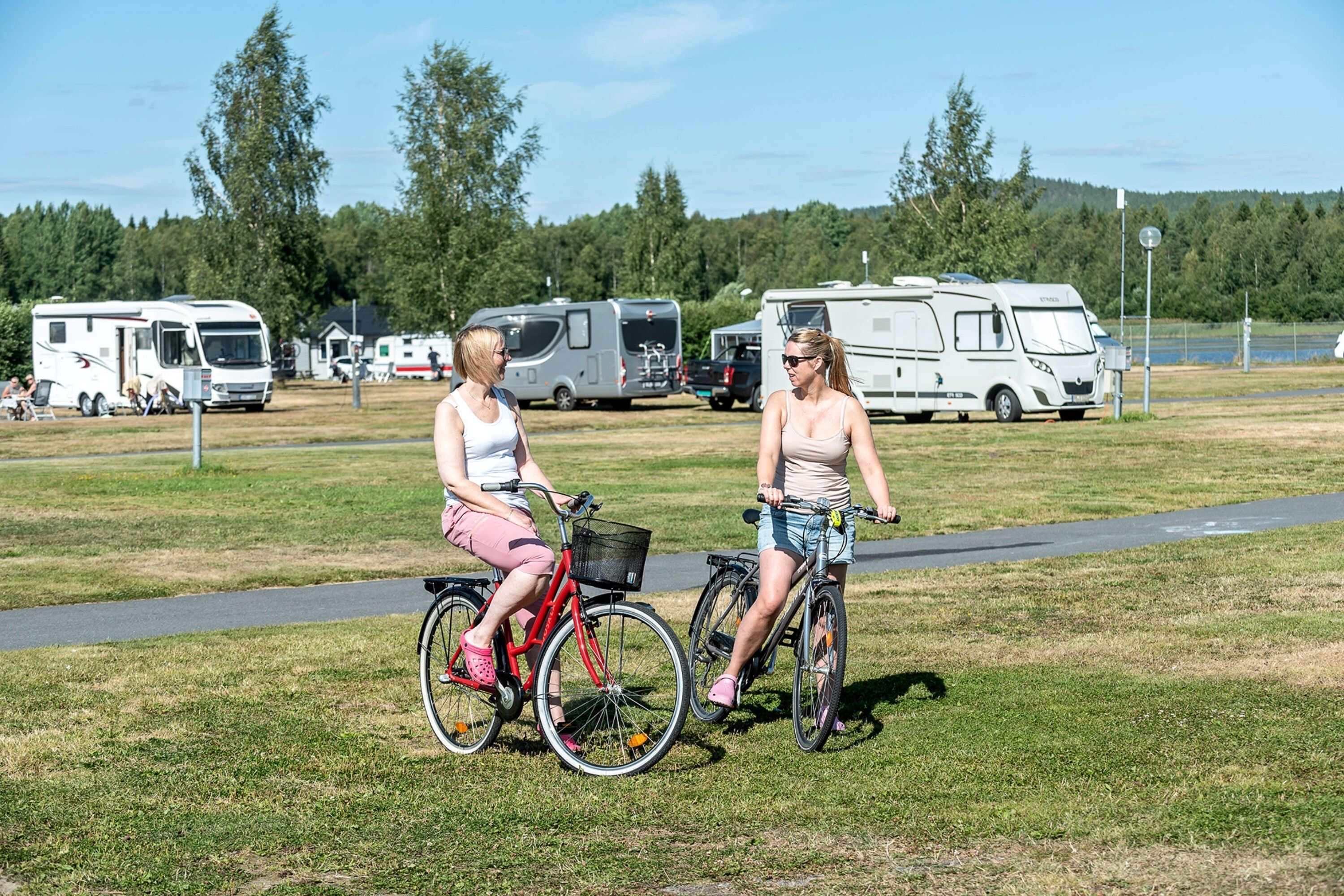 Two people on bicycles in a grassy area with RVs in the background.