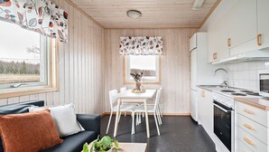 Cocina compacta con gabinetes blancos y una estufa, comedor con una mesa y sillas, y un sofá con un cojín.