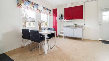 Un comedor con mesa y sillas, una cocina con armarios rojos y una ventana con vista a casas.