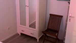 A room with a white wardrobe, a wooden chair, and a painting on the wall.