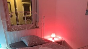 A single bed with a metal frame, a bedside table, and a nightstand with a lamp.