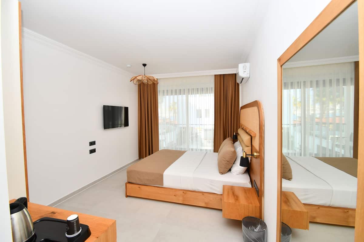 A modern hotel room with a wooden bed, a flat-screen TV, a coffee machine, and a large mirror.