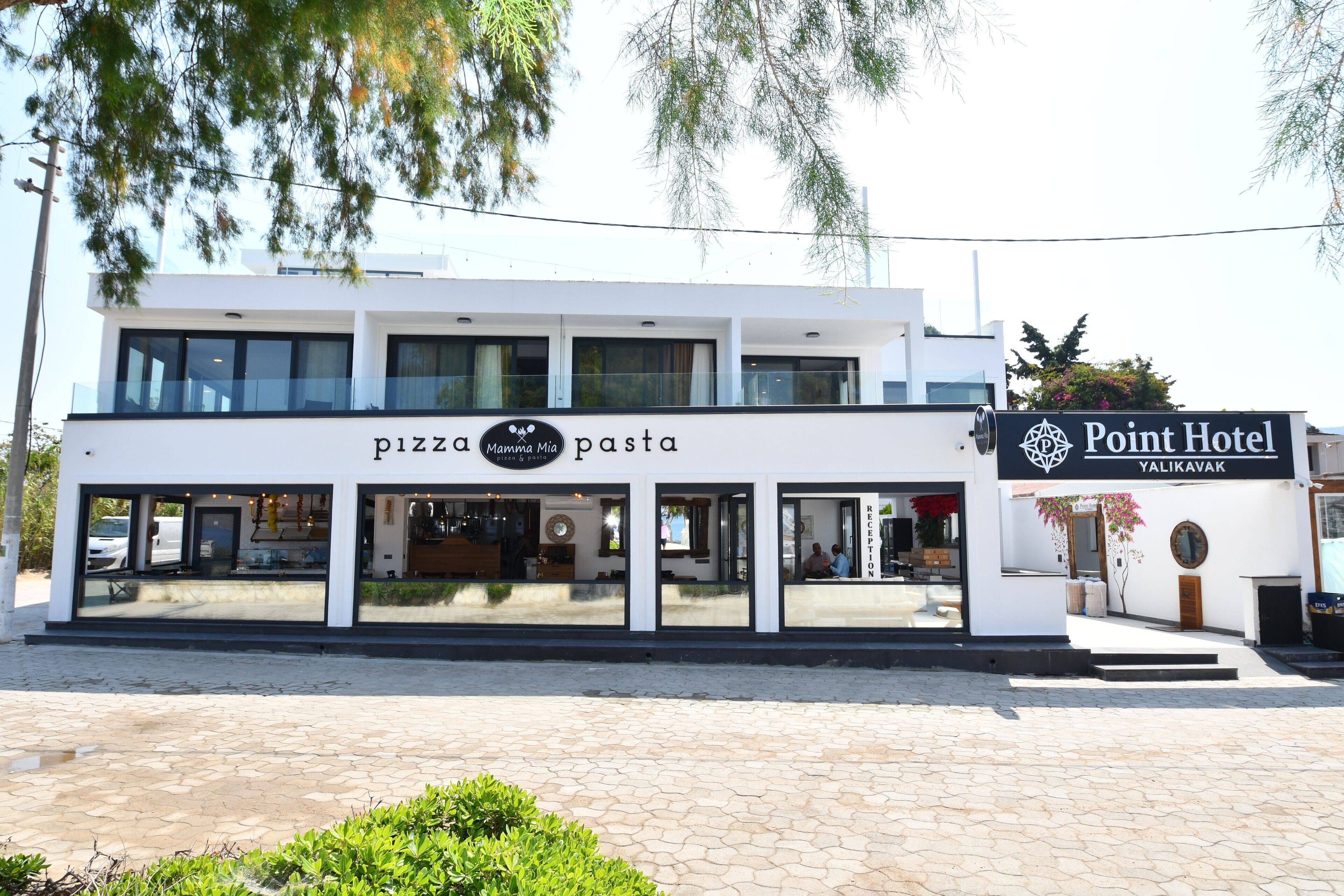 Een modern gebouw met een restaurant dat pizza en pasta serveert, en een hotel genaamd Point Hotel Yalikavak.