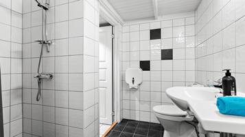 A bathroom with white tiled walls, a black tiled floor, a shower, a toilet, and a sink with a blue towel.