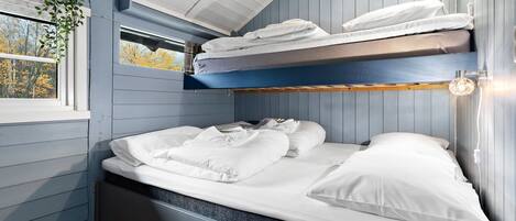 A bunk bed with white bedding, a window with a view of autumn trees, and a plant hanging from the ceiling.