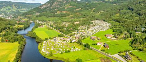 Vista aérea de un pequeño pueblo con un río, campos verdes y un grupo de casas.