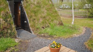 Eine kleine, geschlossene Struktur mit Holztür, ein Kiesweg dorthin und eine Holzterrasse mit einem Blumentopf.