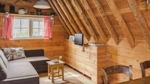 Ein gemütliches Holzhaus mit geneigter Decke, einer Couch, einem kleinen Tisch und einem Fernseher.
