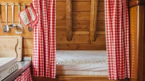 Ein Holzblockhaus-Interieur mit einem Bett, einer Holzwand und roten sowie weißen Karottenvorhängen.