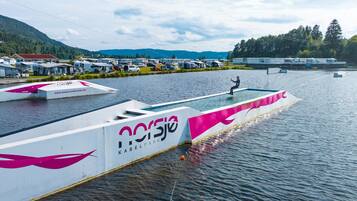 A water-based recreational area with a white structure featuring the text "Norsjo KABELPARK" and a person standing on a platform.