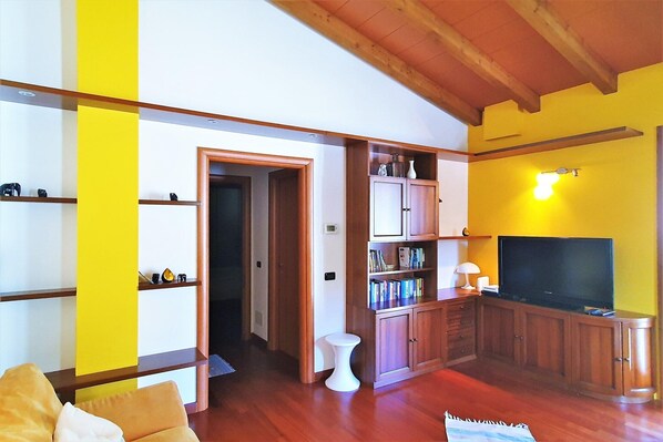 Una sala de estar con pisos de madera, televisor, estanterías y un taburete blanco.