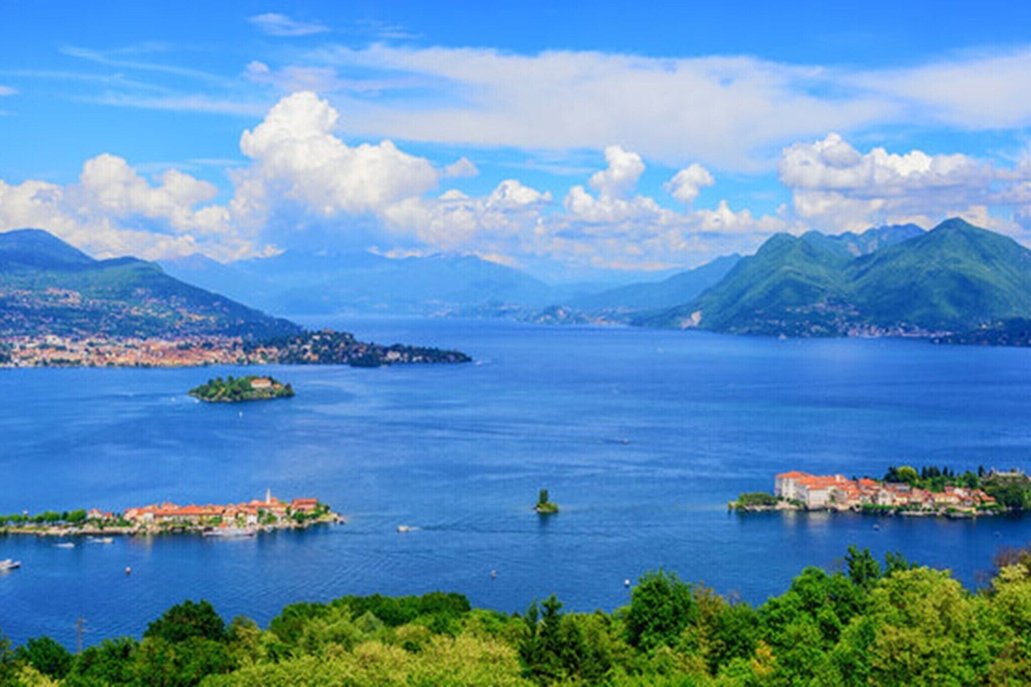 Vista panorámica de un pueblo costero con una extensa masa de agua, varias islas y montañas al fondo.
