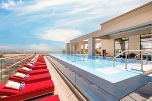 A rooftop pool with red lounge chairs and a clear view of the city skyline. - Agora, Doha, Autograph Collection (Lusail)