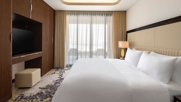 A hotel room with a large bed, a TV, a desk, and a view of the outdoors. - Agora, Doha, Autograph Collection (Lusail)