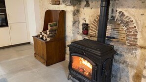 Una estufa de leña con fuego encendido, un mueble de madera con un cartel, y una pared de piedra con una chimenea.