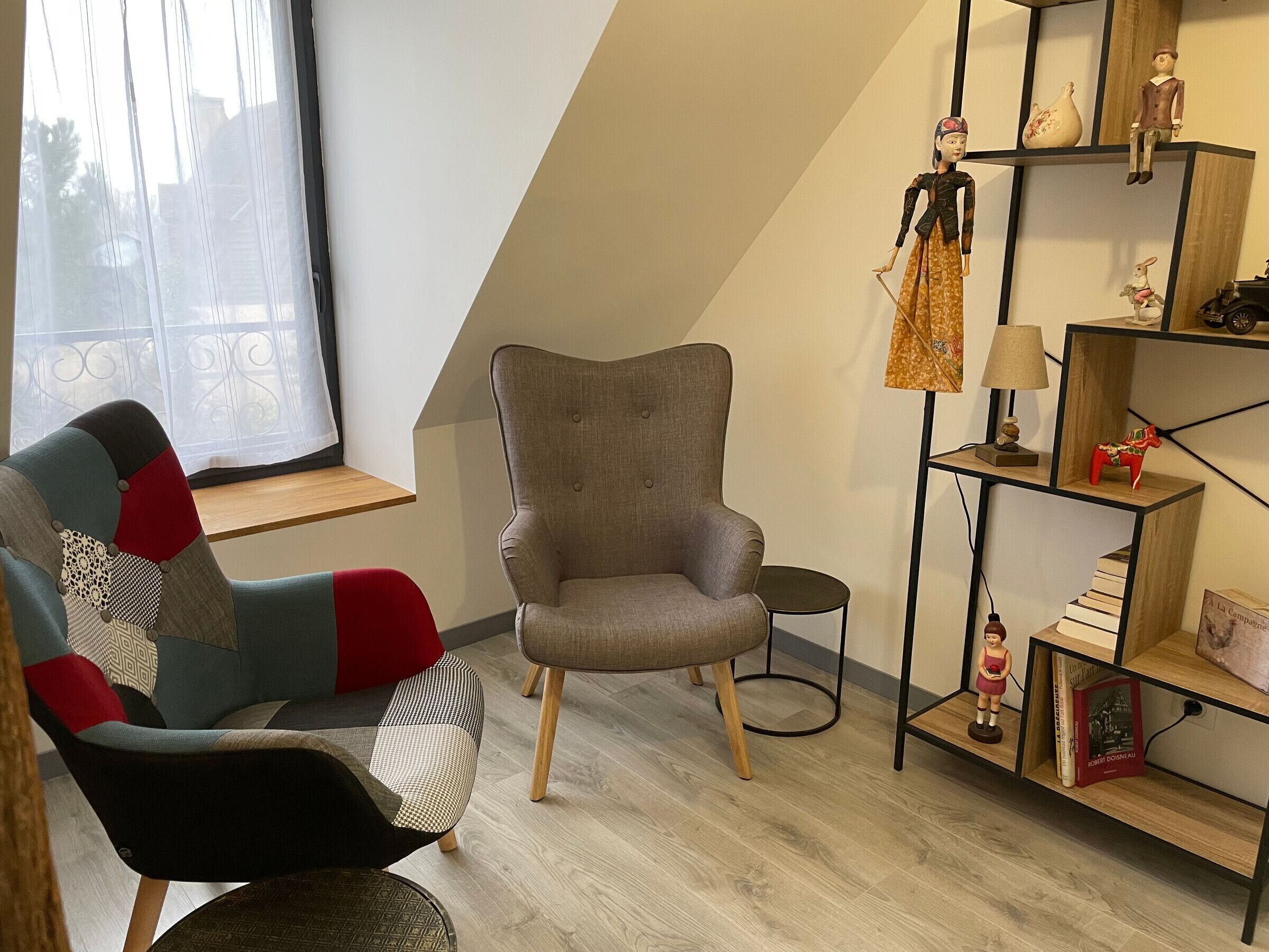 Ein modernes Wohnzimmer mit einem grauen Sessel, einem farbenfrohen Sessel, einem Holzregal und einem kleinen Tisch.