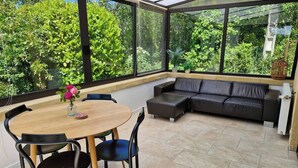 Un patio soleado con una mesa redonda de madera, sillas negras y un sofá de cuero oscuro.
