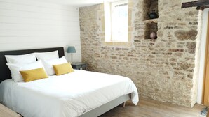 Un dormitorio con pared de piedra, suelo de madera y cama con ropa de cama blanca y almohadas amarillas.