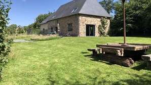 Una casa de piedra con techo inclinado, una terraza de madera y un poste de metal.