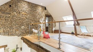 Un loft espacioso con pared de piedra, un entrepiso de madera y un tragaluz grande.