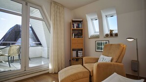 Een kamer met een groot raam, een boekenkast, een stoel en een vloerlamp.