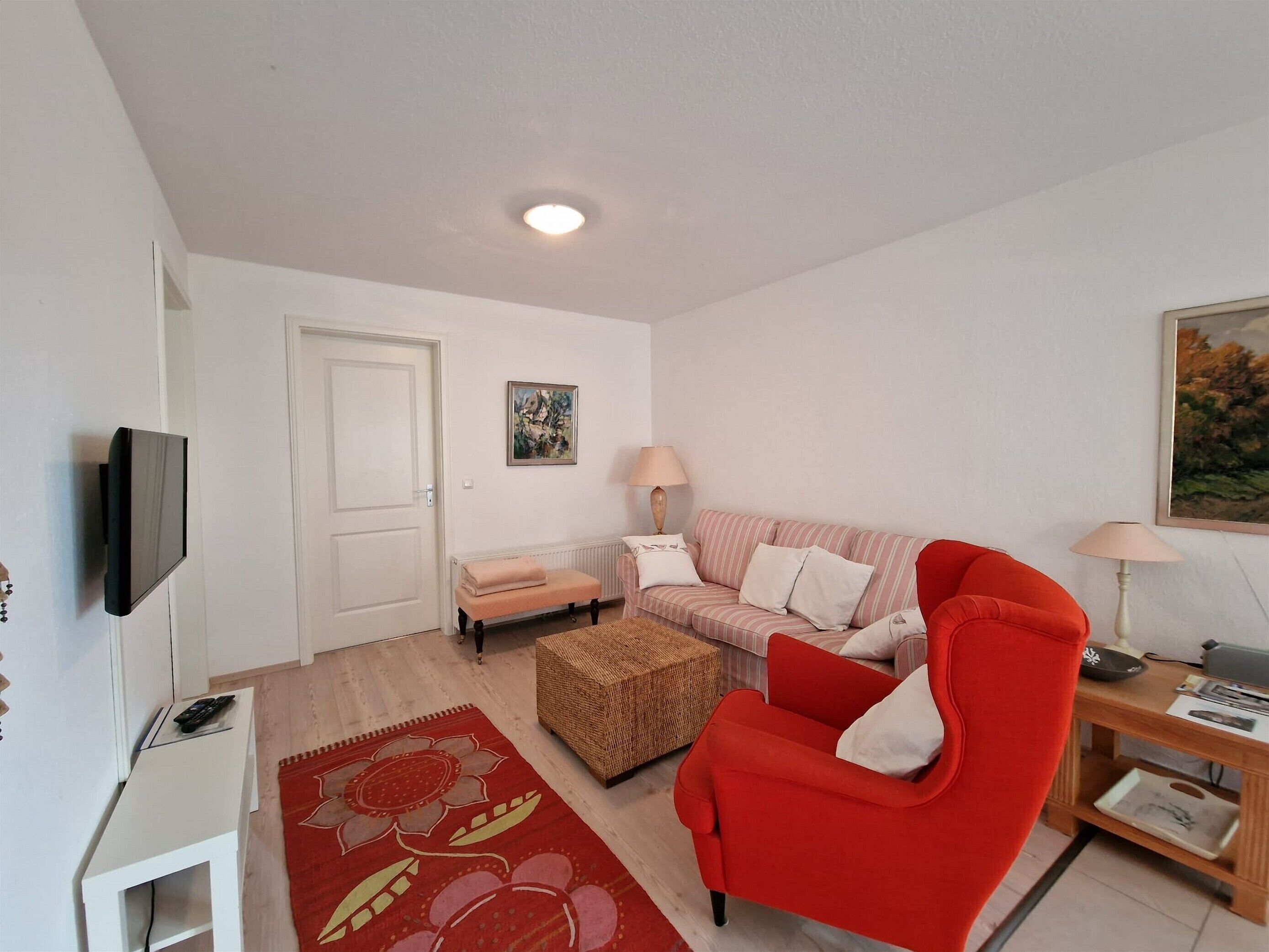 A living room with a red armchair, a sofa, a bench, a TV, and a painting on the wall.