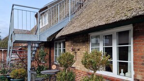 Une maison en briques avec un toit de chaume, un escalier en métal et un petit espace extérieur aménagé avec des tables et des chaises.