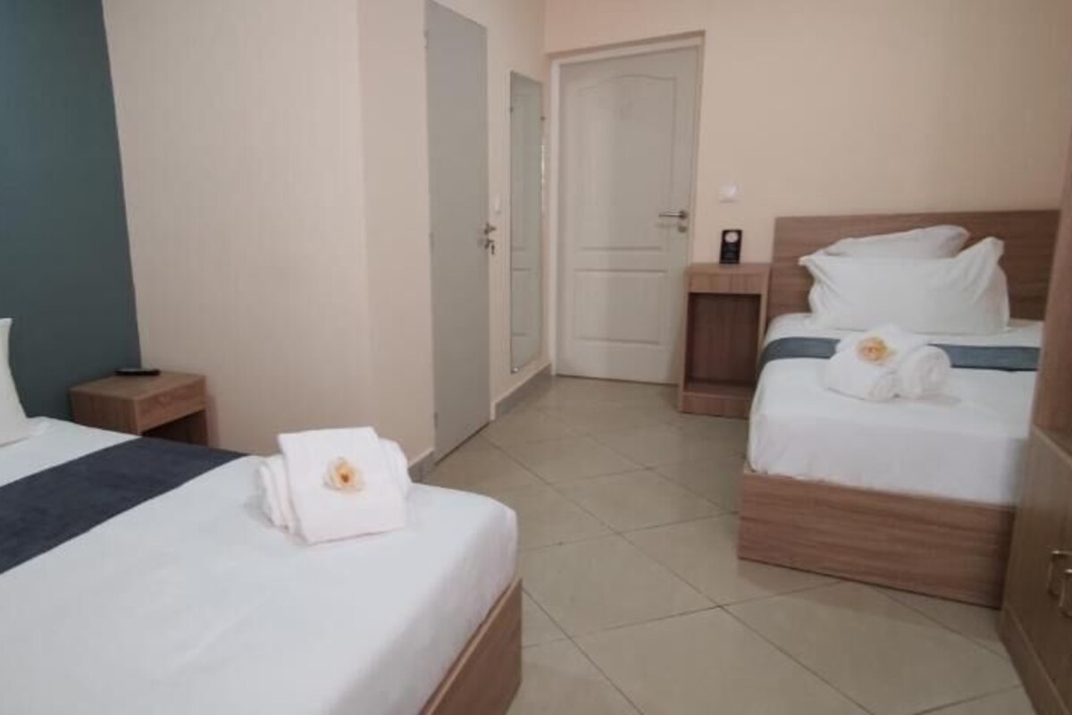Une chambre d’hôtel avec deux lits, une table de chevet, une armoire en bois et une porte donnant sur une autre pièce.