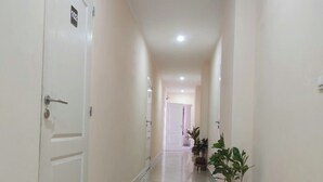 A clean, well-lit hallway with white walls and tiled flooring, leading to a door marked with the number 102. - DOWNTOWN HOTEL (Antananarivo)