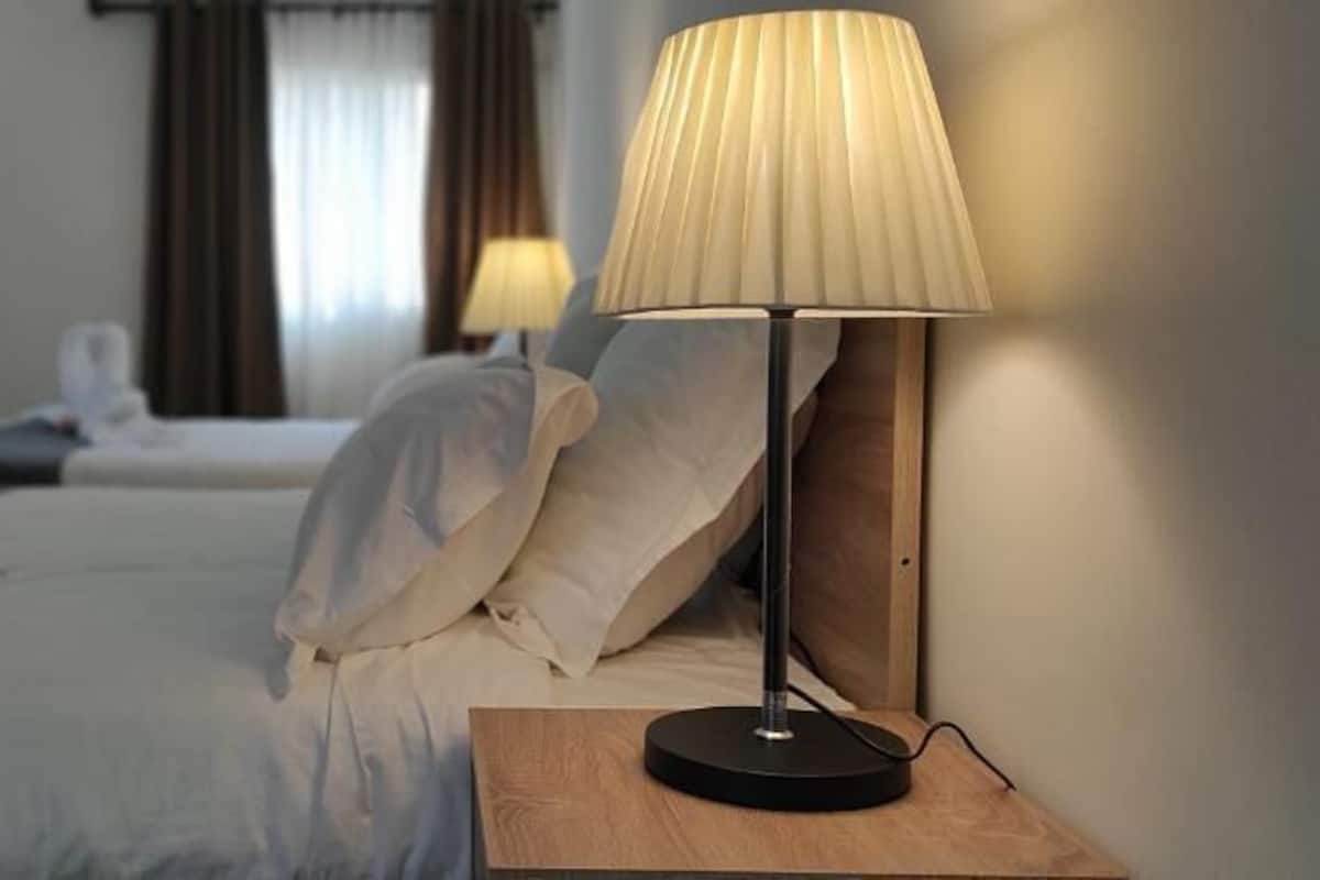 Een hotelkamer met twee bedden, een nachtkastje met een lamp en uitzicht op de straat.