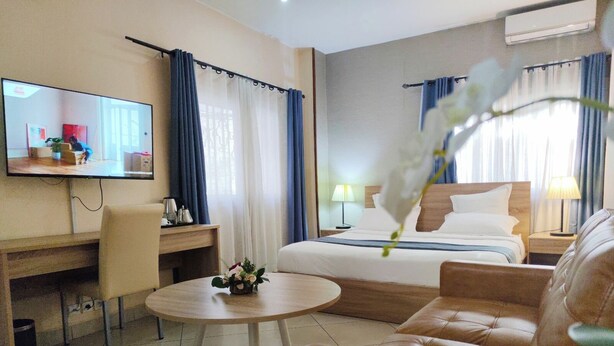 A hotel room with a bed, a desk, a chair, a round table, a TV, and a flower arrangement. - DOWNTOWN HOTEL (Antananarivo)