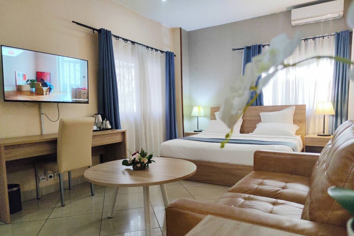 Hotelkamer met een bed, bureau, stoel, ronde tafel, televisie en bloemstuk.