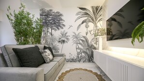 Una sala de estar moderna con un sofá gris, un tapete tejido y un mural de plantas tropicales.