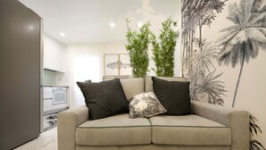 Un sofá color beige con detalles verdes, dos almohadas oscuras y una almohada estampada.