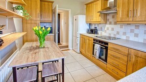 Een moderne keuken met houten kastjes, een ingebouwde oven en een eettafel met stoelen.