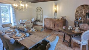 Een rustieke eethoek met een houten tafel gedekt voor vier personen, omringd door gestoffeerde stoelen. Een kroonluchter hangt aan het plafond, en een grote spiegel weerspiegelt de ruimte.