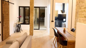 Ein modernes Wohnzimmer mit einer Couch, einem Esstisch mit Stühlen, einer Schiebetür und einer sichtbaren Küche durch eine offene Tür.