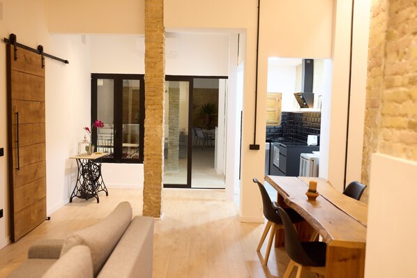 A modern living room with a sofa, a dining table with chairs, a sliding door, and a kitchen visible through an open door. - PR27 RUZAFA APARTMENT WITH 50 M TERRACE AND SMALL POOL (València)